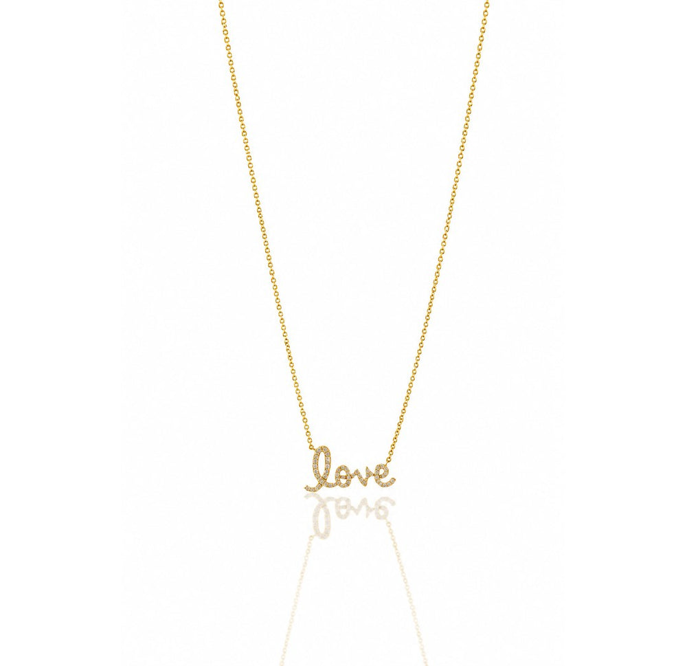 A delicate gold chain necklace featuring a small cursive pendant spelling 'love', displayed against a clean white background with a soft reflection below.
