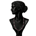 A black classical-style bust wearing a delicate necklace with alternating pink gemstones and silver-toned floral motifs,